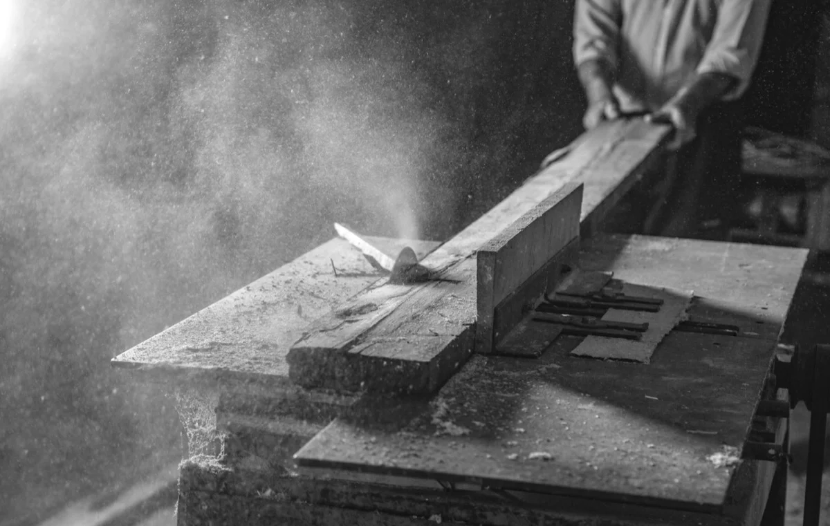 Craftsman working with table saw, sawdust in the light