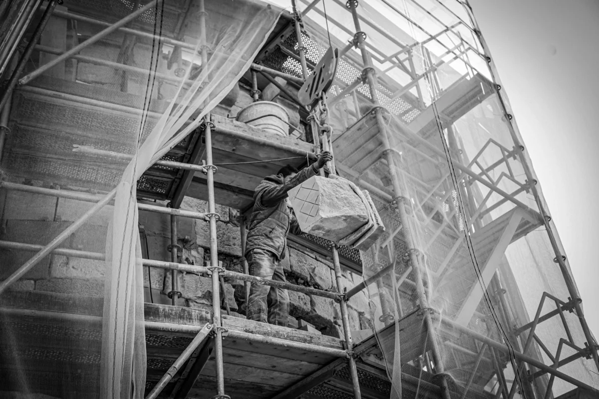 Mason working on scaffold, restoring a historic stone building